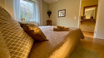 A bedroom with a large bed, a window with curtains, a framed picture on the wall, and a mirror in the adjacent room.