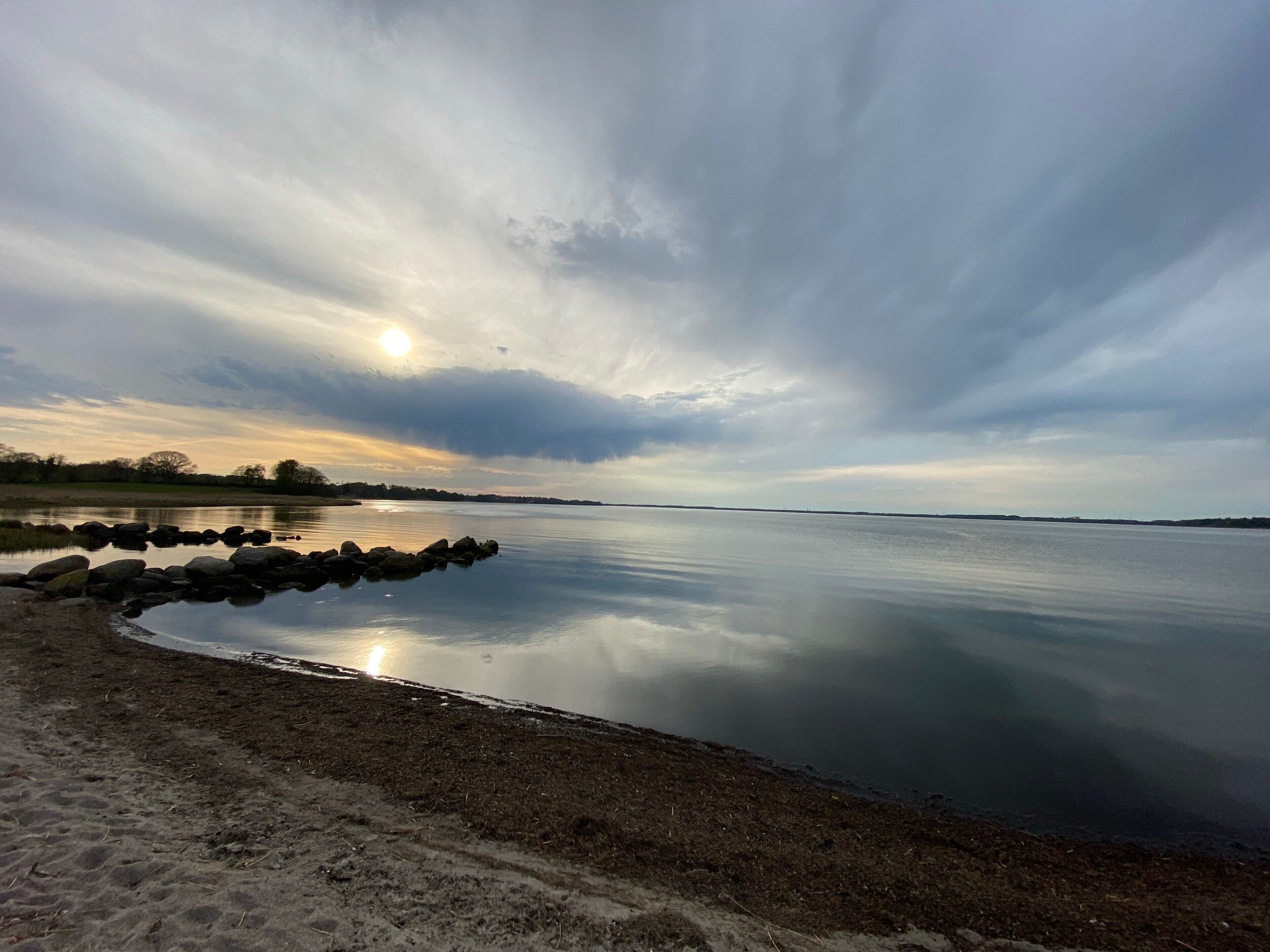 A calm lake with a rocky shoreline and a clear sky.