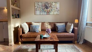 A living room with a brown leather sofa, striped pillows, a wooden coffee table, and a decorative painting on the wall.
