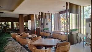 A spacious dining area with a large wooden table surrounded by wicker chairs, a patterned floor, and vertical wooden slats on the walls. - Sekuro Village Beach Resort (Mlonggo)