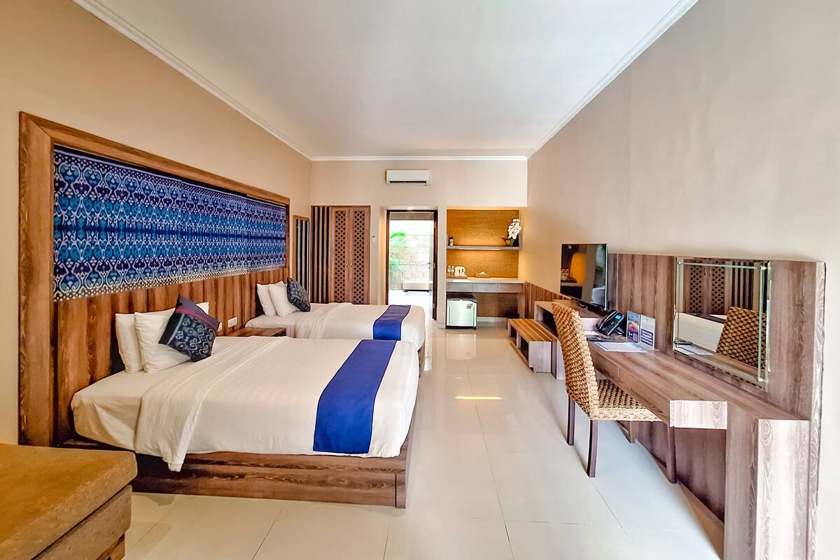 A hotel room with two beds, a kitchenette, a TV, and a seating area.