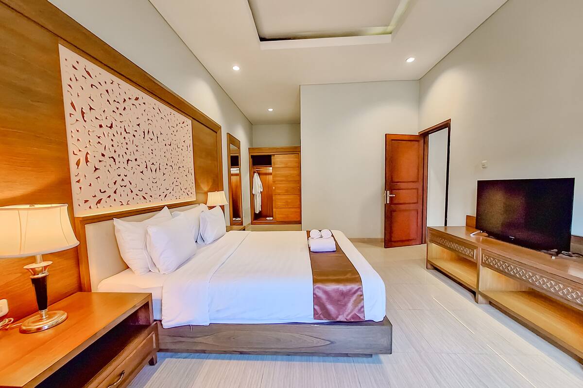 A hotel room with a large bed, a TV, a wooden desk, and a wardrobe.