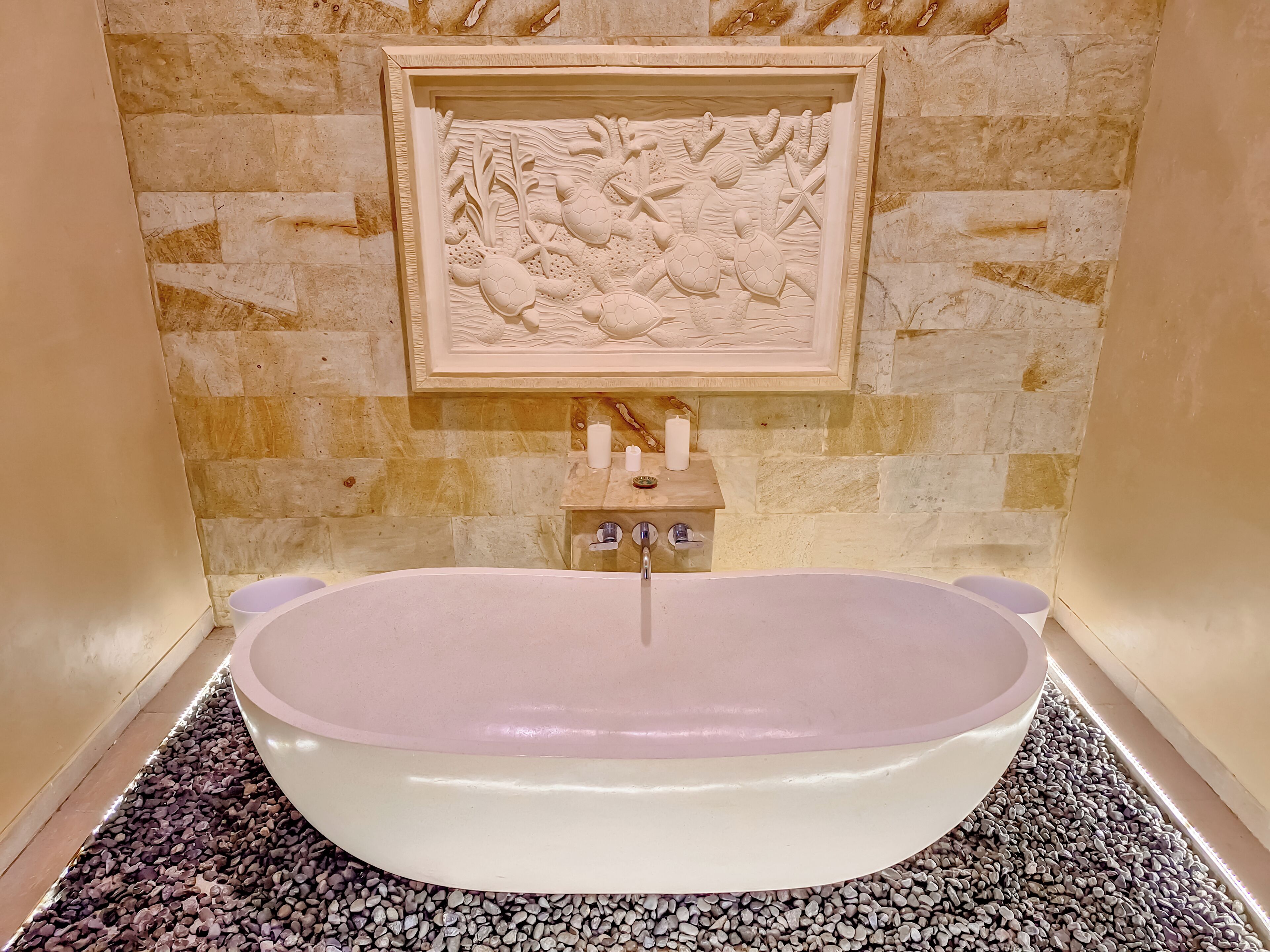 A bathroom with a freestanding bathtub, a stone wall, and a framed artwork above the sink.