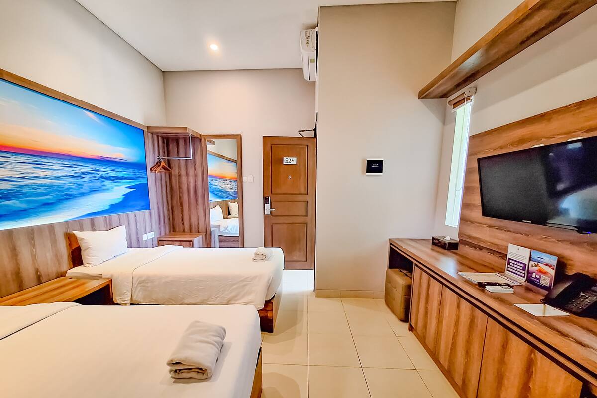 A hotel room with two beds, a TV, and a painting of a beach scene.