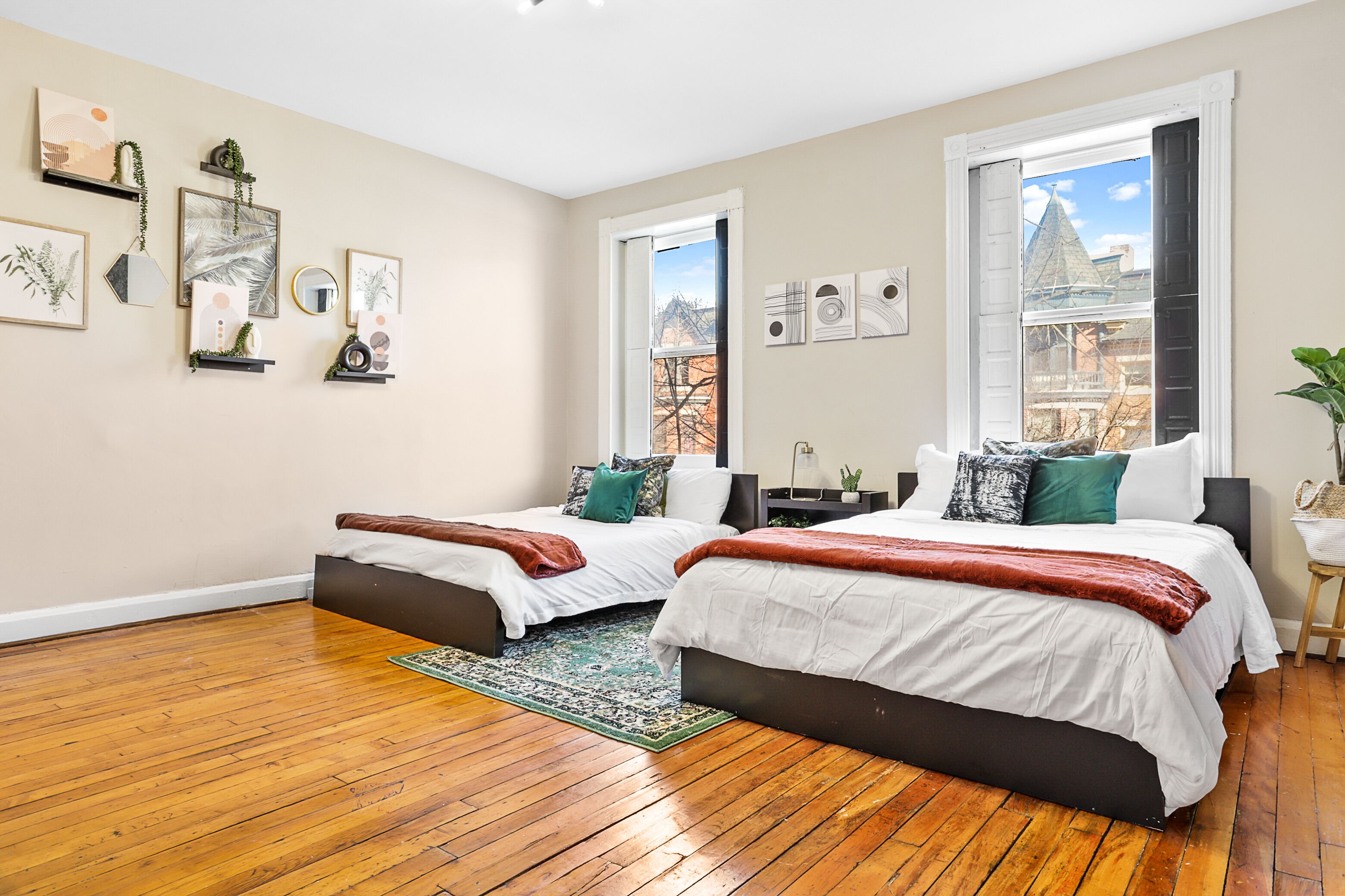 Quarto moderno com duas camas, piso de madeira e vista para a cidade através de grandes janelas.