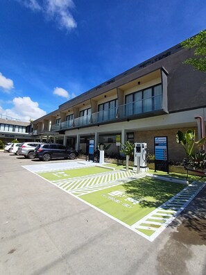 A building with a parking lot, EV charging stations, and a sign for a cafe. - Prince Express Inn Bogo City Cebu (Bogo)