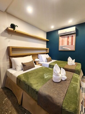 A hotel room with two beds, a wooden headboard, a wall-mounted air conditioner, and a framed picture.
