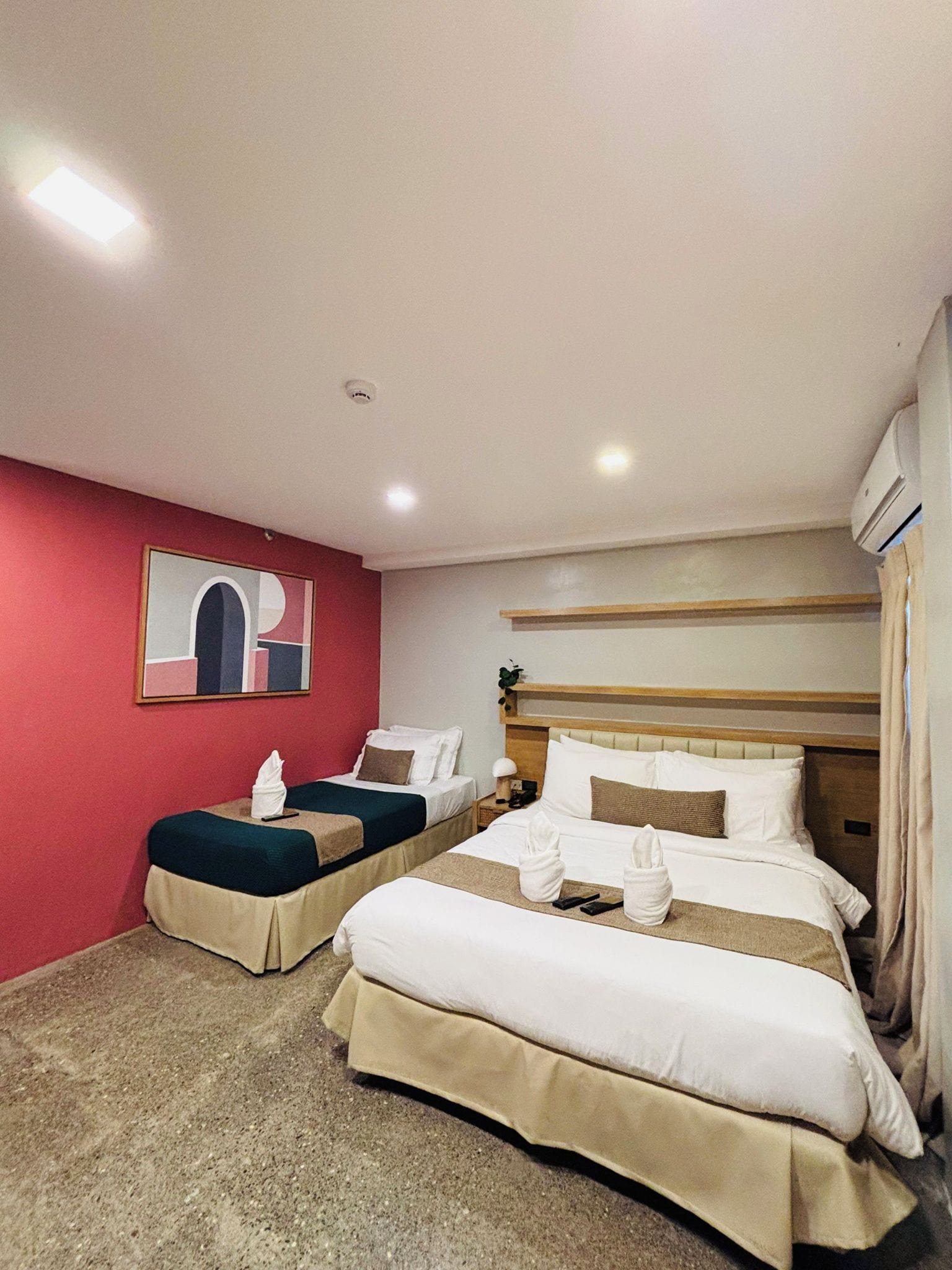 A hotel room with two beds, a red accent wall, and a painting.