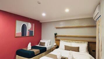 A hotel room with two beds, a red accent wall, and a painting.