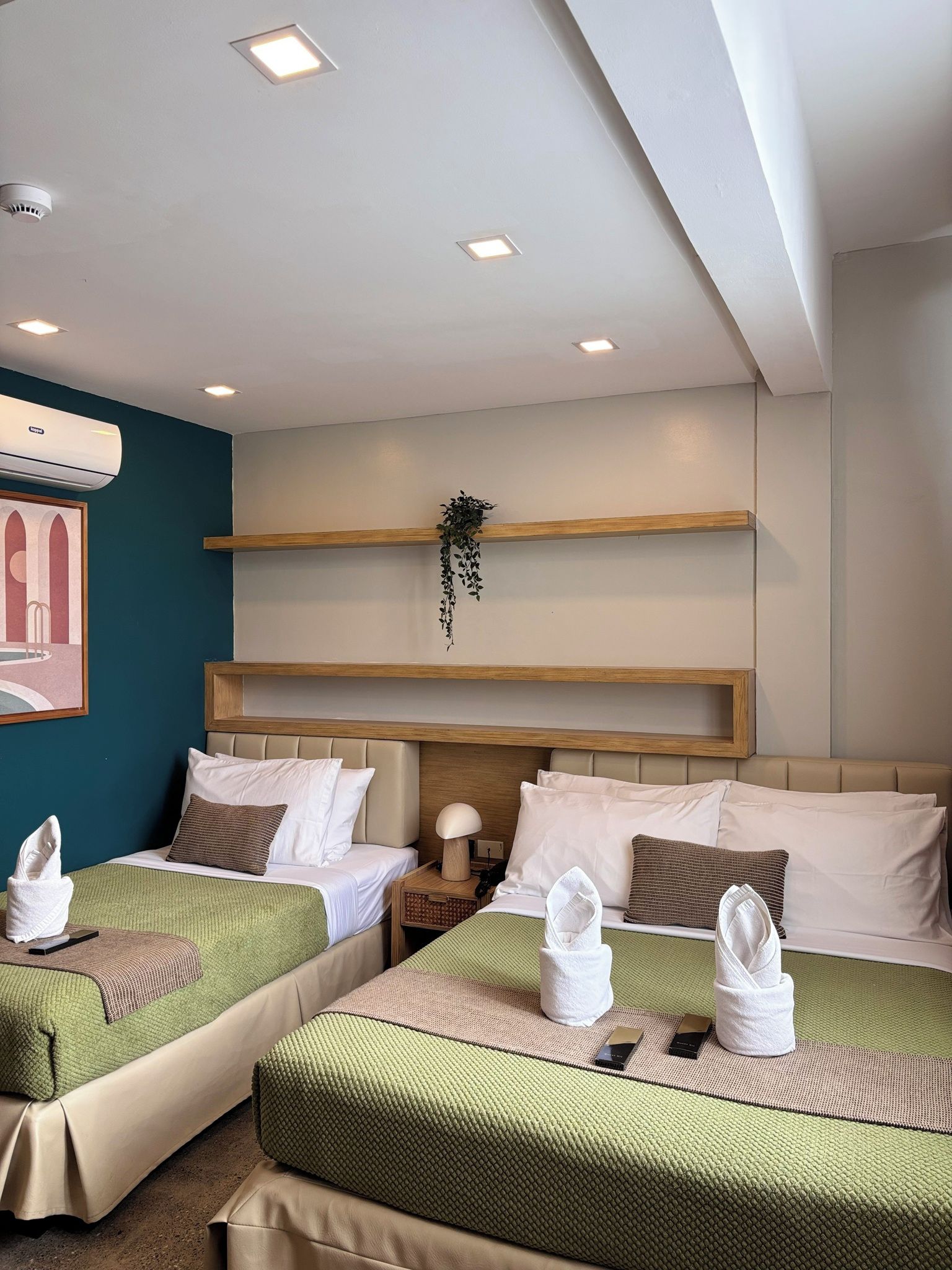 Habitació d'hotel amb dos llits, aire condicionat fixat a la paret, un quadre amb marc i una planta.