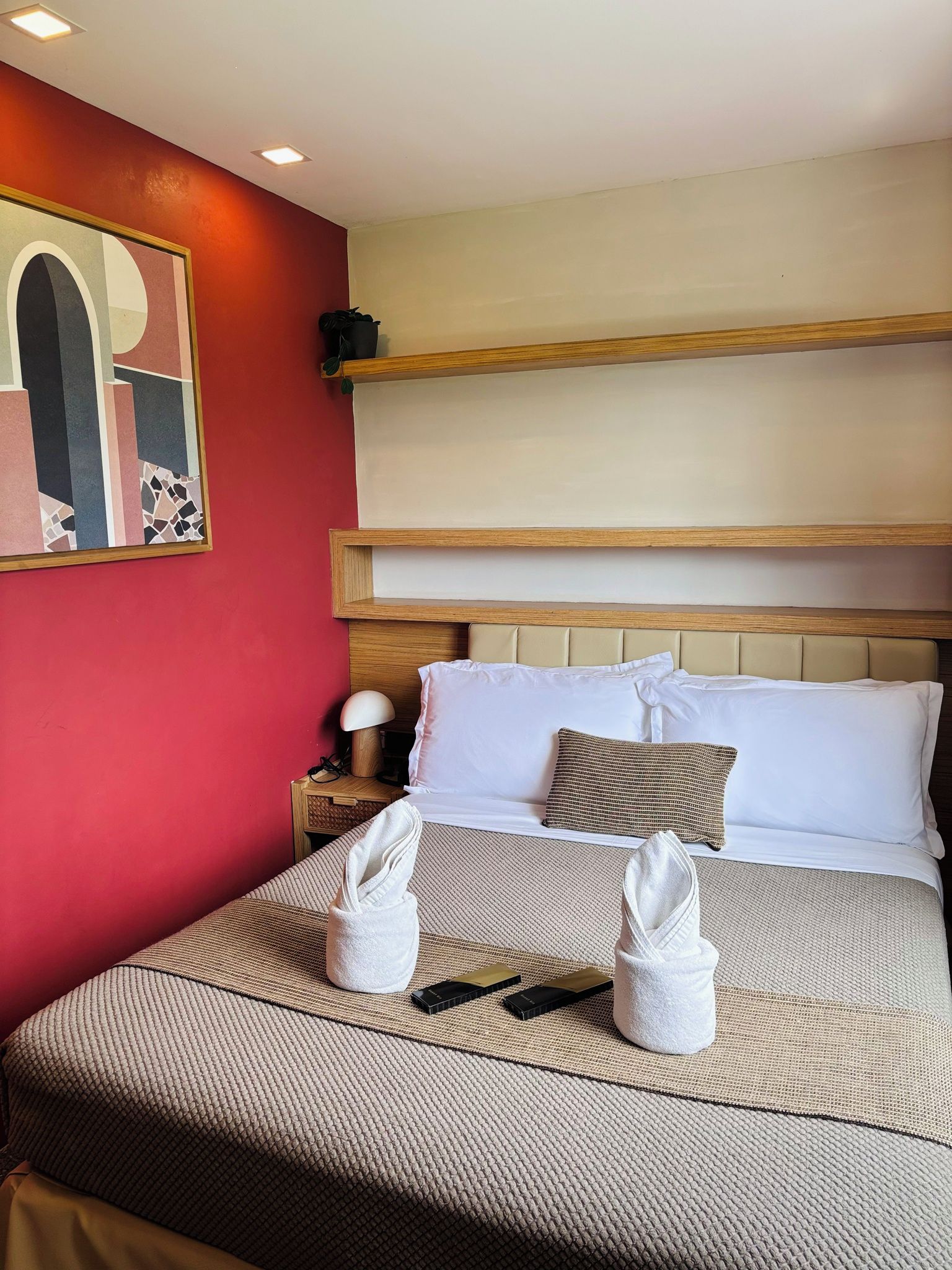 A hotel room with a bed, a nightstand, a lamp, and a painting on the wall.