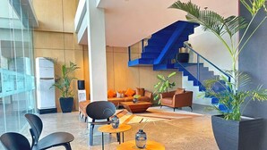 A modern lobby with a staircase, seating area, and potted plants.