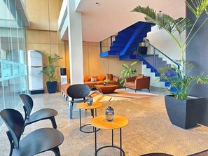A modern lobby with a staircase, seating area, and potted plants.