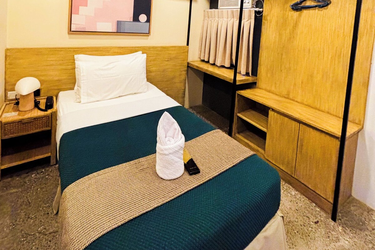 A hotel room with a bed, a bedside table, a nightstand, a wardrobe, a mirror, and a wall-mounted artwork.