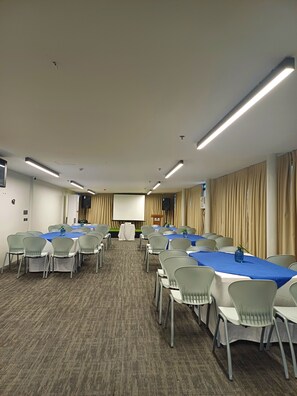 A conference room with multiple tables and chairs, a projector screen, and a speaker system. - Prince Express Inn Bogo City Cebu (Bogo)
