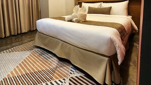 A hotel room with a bed, a bedside table, a wall-mounted shelf, and a large window with curtains.