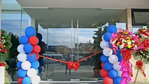 Une entrée avec une porte en verre, agrémentée d’une cérémonie de coupe du ruban rouge, le tout entouré de ballons et de compositions florales.