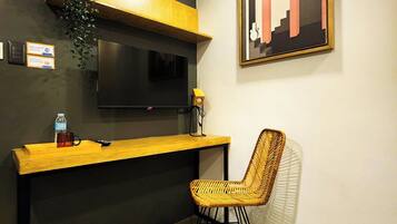 A modern room with a wooden desk, a television mounted on the wall, a wicker chair, and a framed artwork.