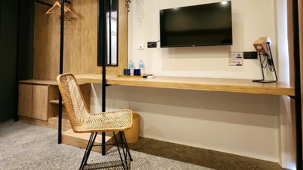 Une chambre moderne avec un bureau en bois, un téléviseur fixé au mur, un fauteuil en osier et une petite plante.
