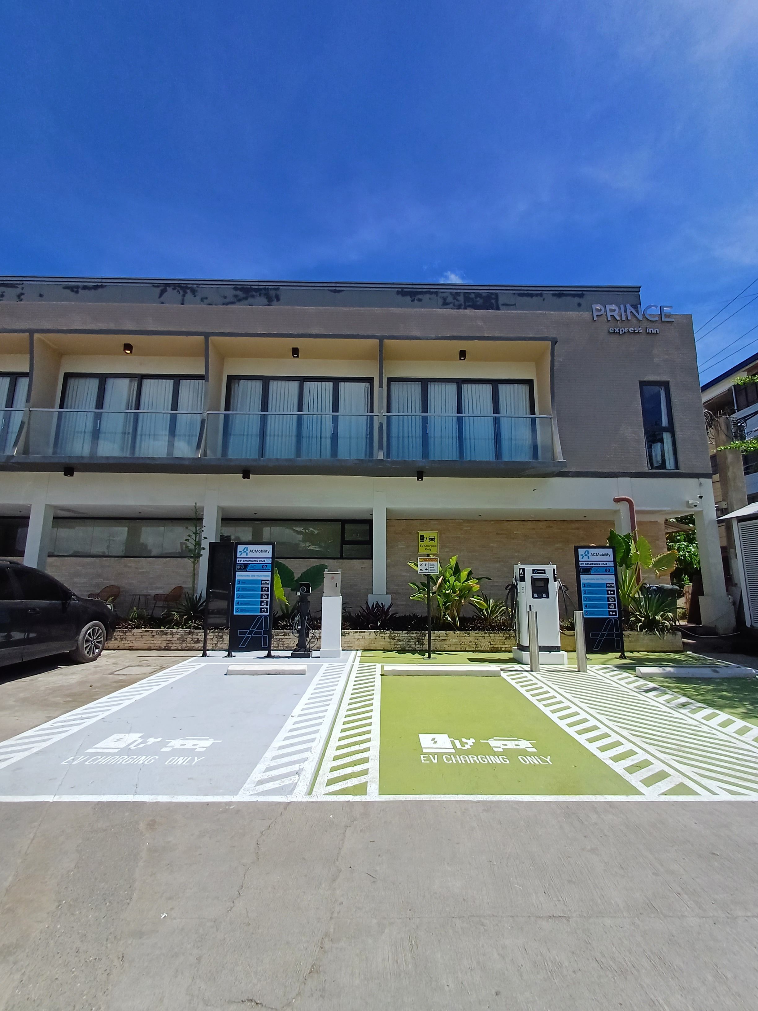 Un hotel con fachada plana, un balcón y estaciones de carga para vehículos eléctricos.