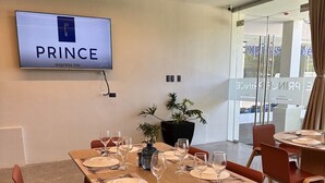 Une salle de conférence de l’hôtel PRINCE Express, avec une grande table préparée pour une réunion, un téléviseur fixé au mur et une plante en pot.