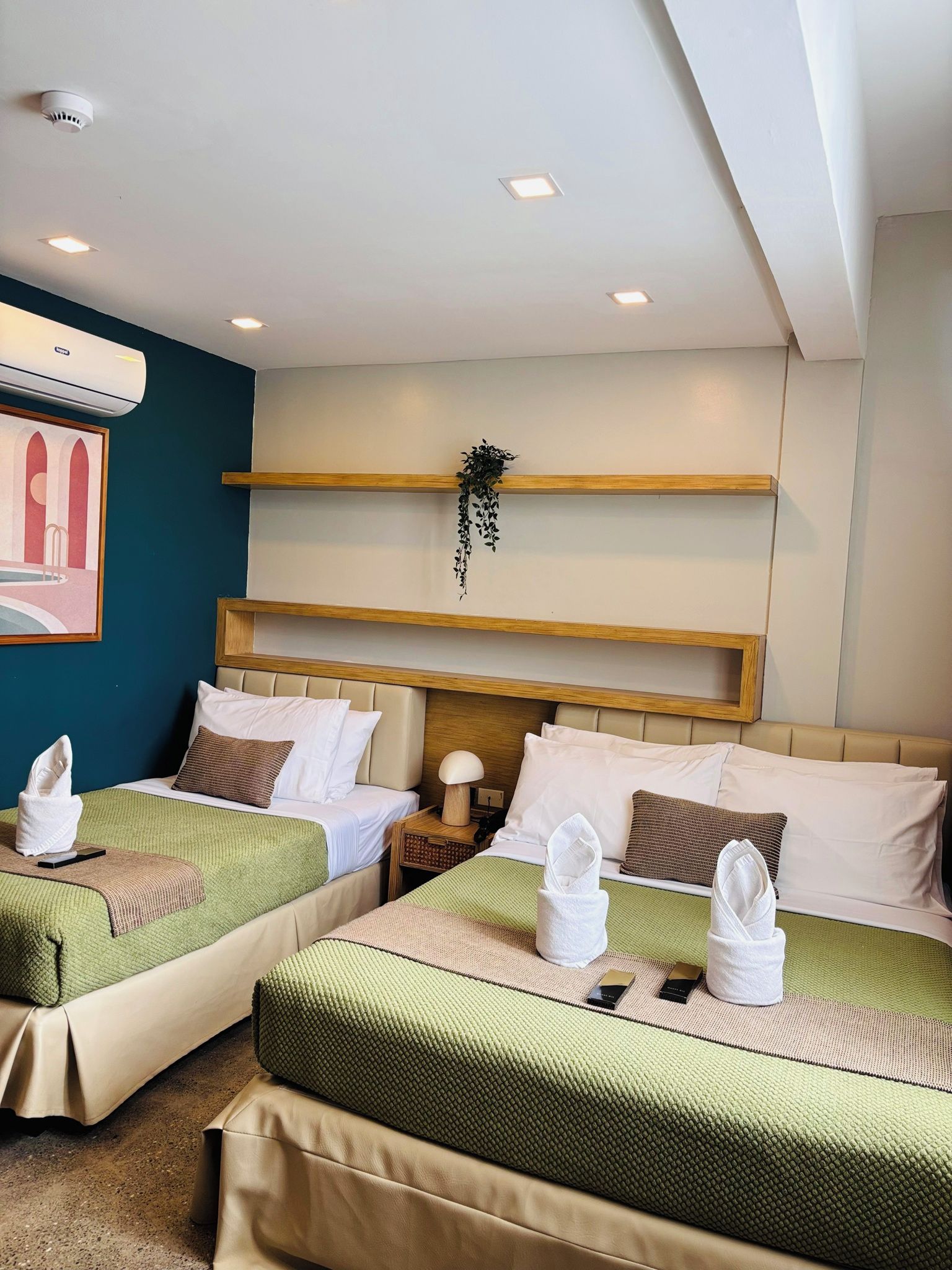 Habitación de hotel con dos camas, aire acondicionado de pared, un cuadro enmarcado y una planta.