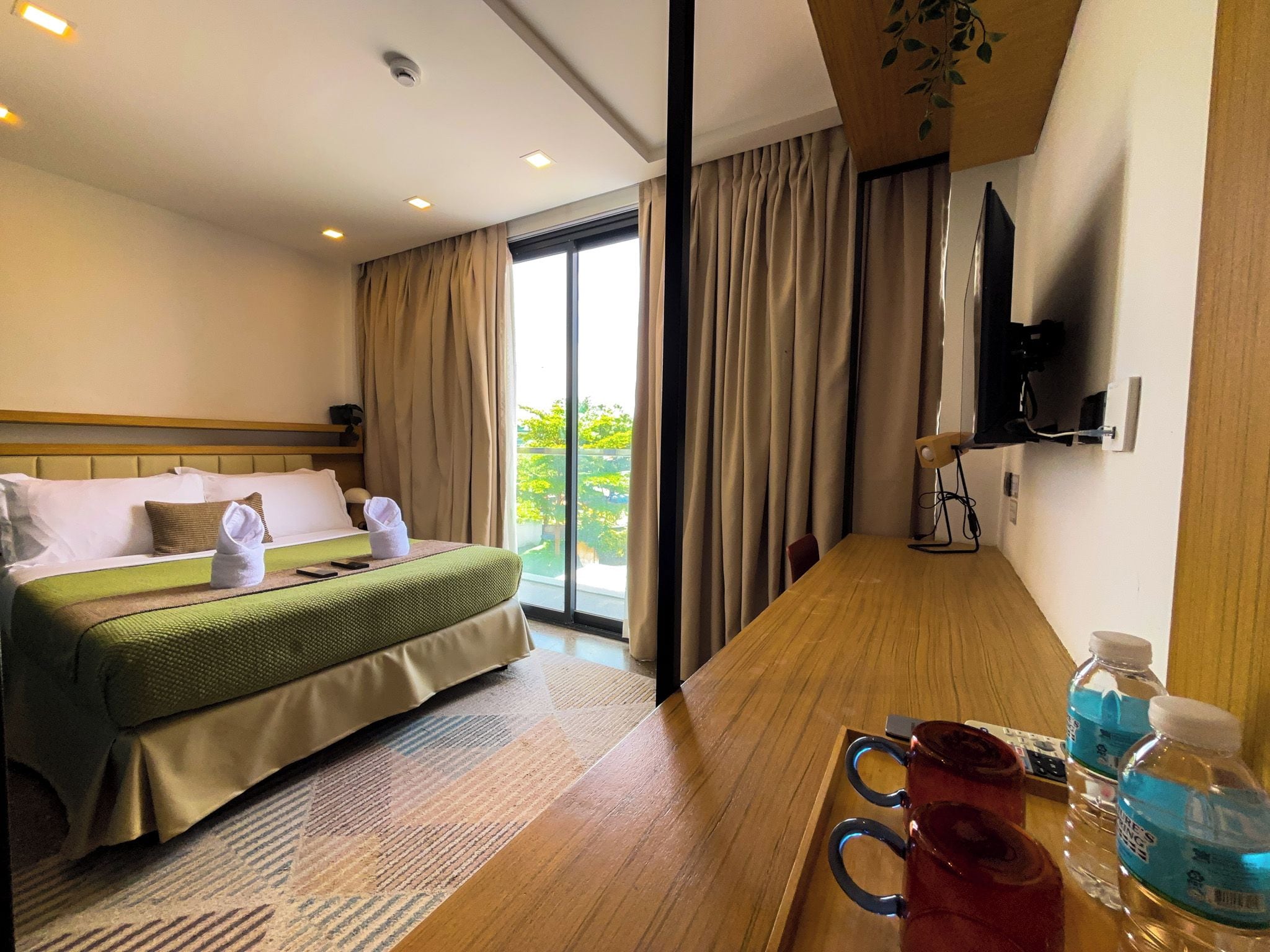 A hotel room with a bed, a wooden desk, a television, and a window with curtains.