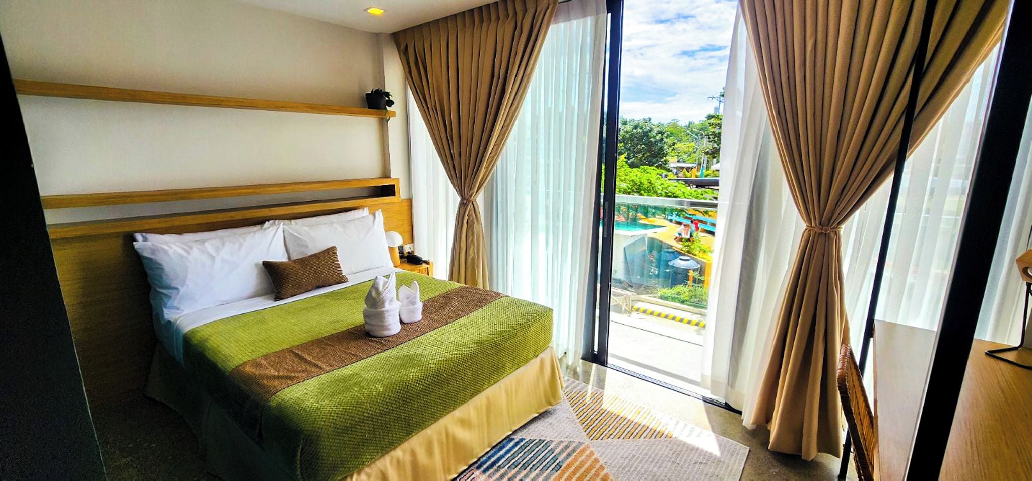 Habitación de hotel con cama, vista a una piscina y cortinas.