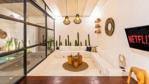 Un salon moderne avec un mur en verre, un canapé blanc, des tables basses en bois et un téléviseur fixé au mur.