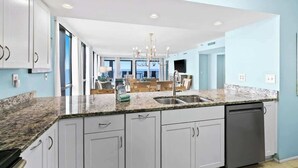 A modern kitchen with granite countertops, white cabinets, and a built-in dishwasher.