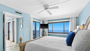 A bedroom with a bed, a ceiling fan, a TV, and a view of the ocean.