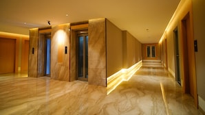 Een moderne hotelgang met marmeren vloeren, houten lambrisering en inbouwverlichting.