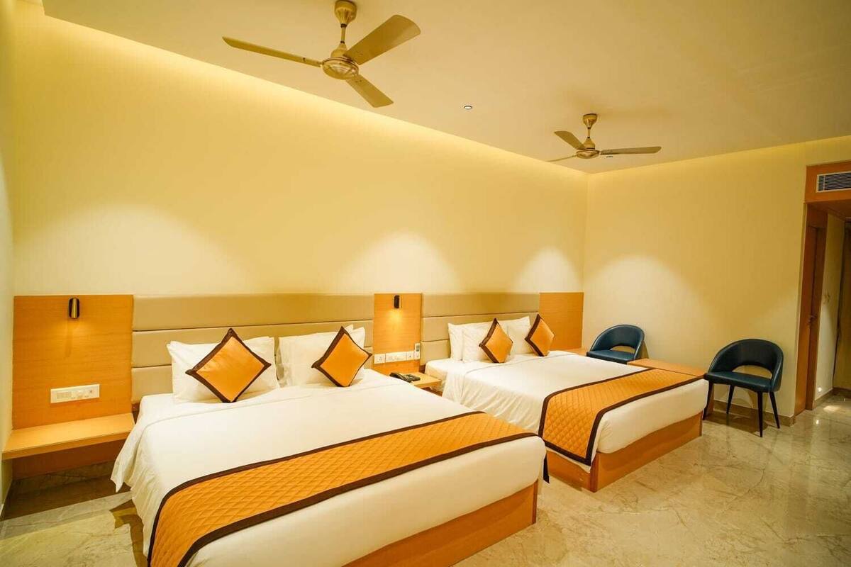 A hotel room with two beds, a desk, a chair, and two ceiling fans.
