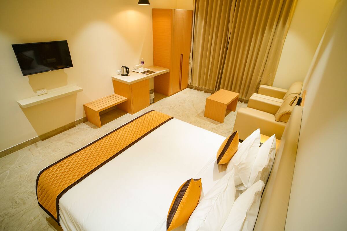 A hotel room with a bed, a desk, a chair, a TV, and a wardrobe.
