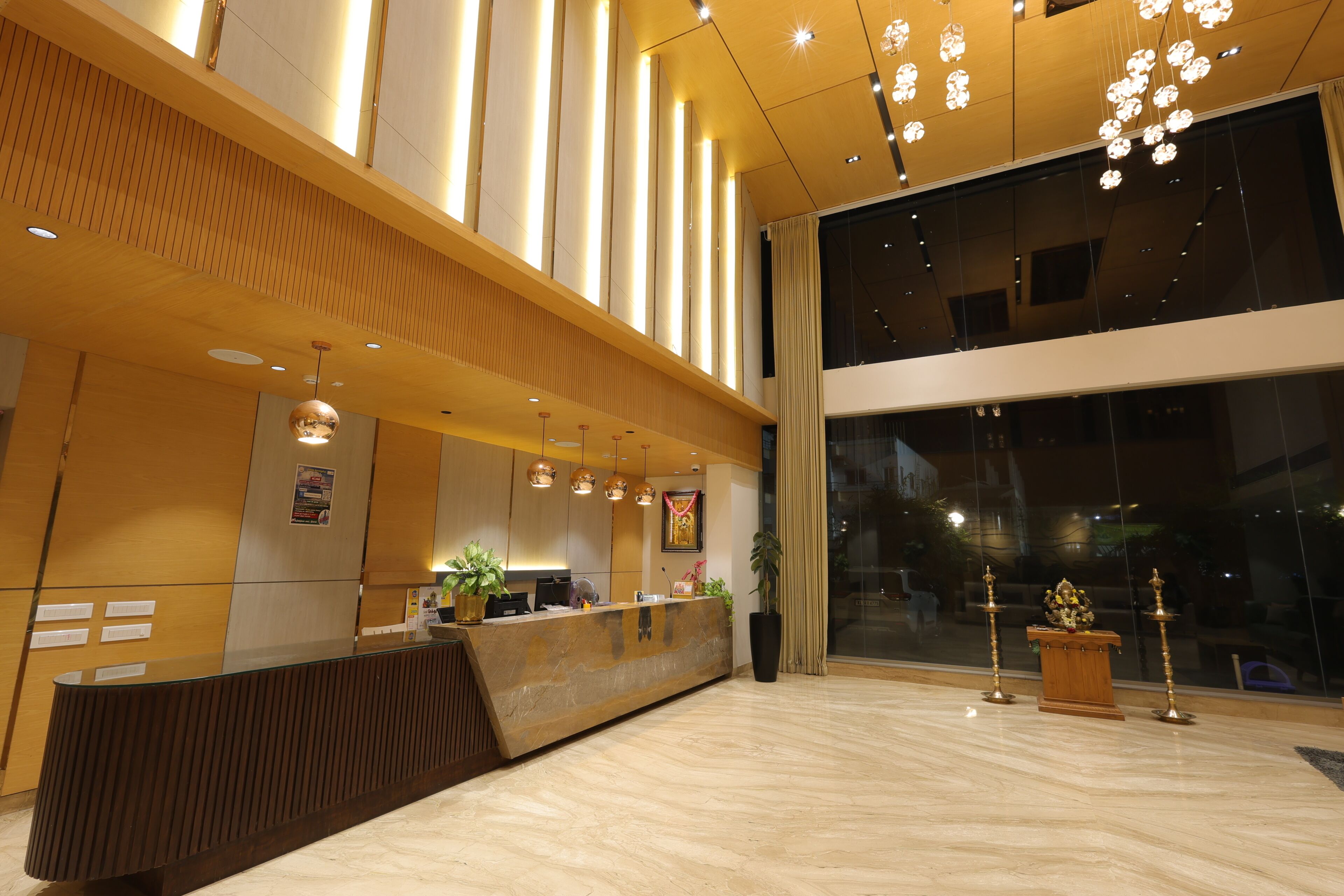 A modern hotel reception area with a wooden reception desk, a large window, and a ceiling with pendant lighting.