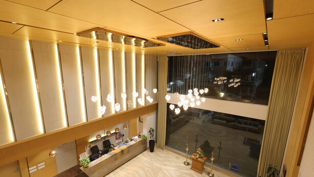 Een hotel receptie met een houten balie, een groot raam met uitzicht op de stad en een moderne kroonluchter.