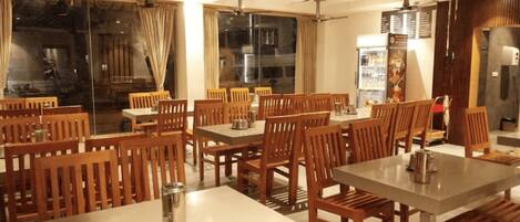 A restaurant with wooden tables and chairs, a ceiling fan, and a large window with curtains.