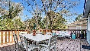 A wooden deck with a white table and chairs, a sofa, and a small table with a vase.