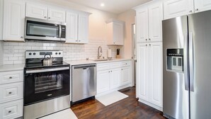 A modern kitchen with white cabinets, stainless steel appliances, and a wooden floor.