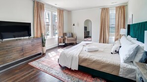 A bedroom with a bed, a TV, a dresser, a chair, and a mirror.