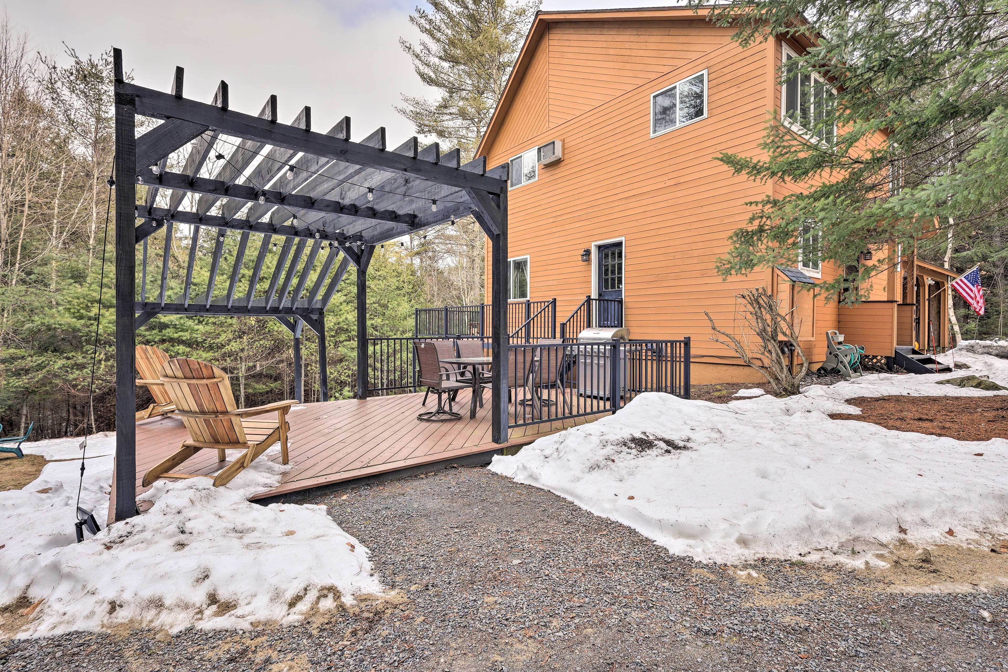 A wooden deck with a pergola, outdoor seating, and a house with a wooden exterior.