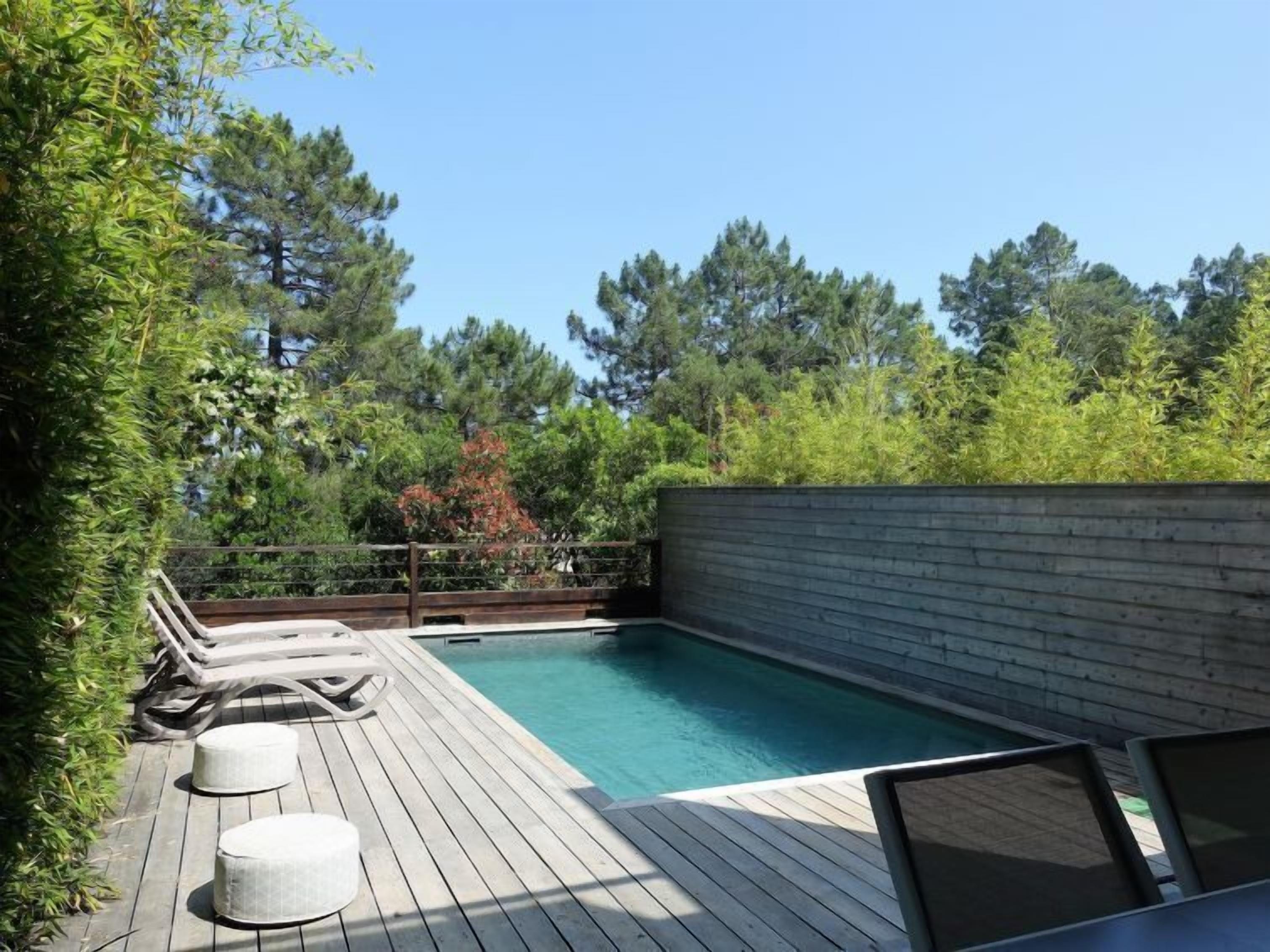 Una terraza de madera con piscina, sillas de descanso y una valla de madera.