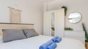 A bedroom with a bed, pillows, a wardrobe, a mirror, and a macrame wall hanging.
