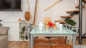 A modern living room with a glass dining table, leather chairs, a flat-screen TV, and a staircase with wooden steps.