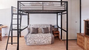 Un lit superposé avec une échelle, un bureau, une lampe et un meuble pour la télévision, dans une pièce au plancher en bois et à la porte blanche.