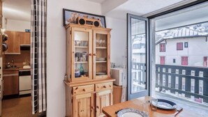 Une cuisine compacte avec des meubles en bois, une table à manger avec de l’assiette, et une vue sur un bâtiment enneigé par le biais d’une grande fenêtre.