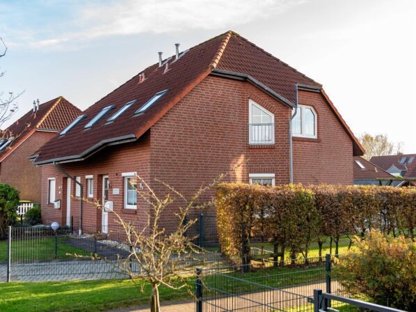 Une maison en briques rouges, avec un toit en pente, de nombreuses fenêtres et une cour clôturée.