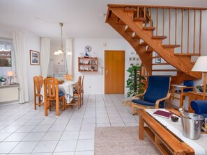 Un salon chaleureux avec un escalier en bois, un coin repas avec des chaises et une table en bois, et une bibliothèque.