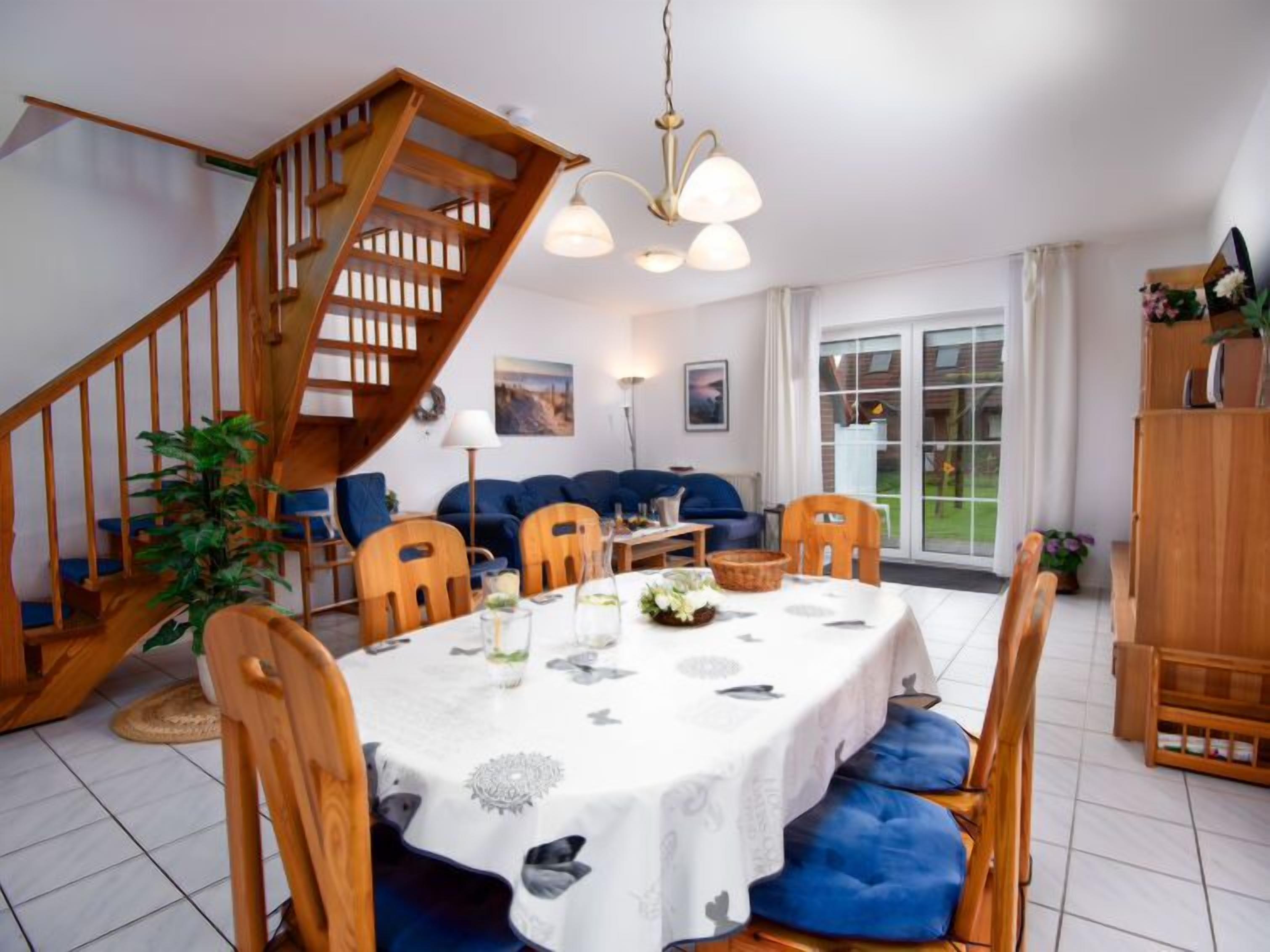 Ein Essbereich mit einer Holztreppe, einem Tisch für vier Personen und einem blauen Sofa im Hintergrund.