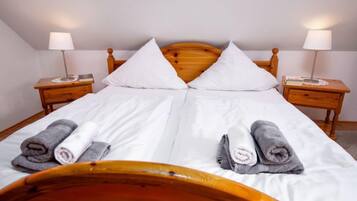 Ein ordentlich bezogenes Bett mit weißen Leinen und zwei Kissen, an beiden Seiten mit Holznachtischen, auf denen Lampen und Bücher stehen.